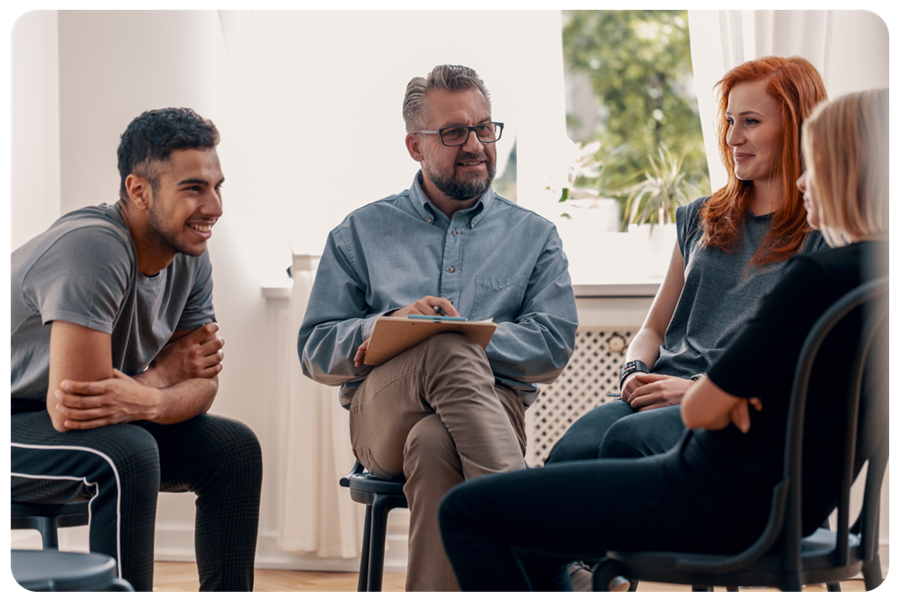 One man and two women talking to a man holding a pen and a clipboard in a group.