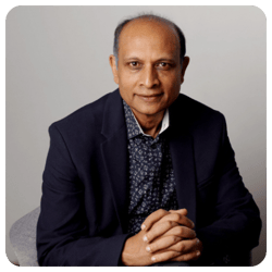 Professional portrait of Dr. Sanjay Rao wearing a dark blazer and patterned shirt, seated with hands clasped, looking calmly at the camera against a neutral background.