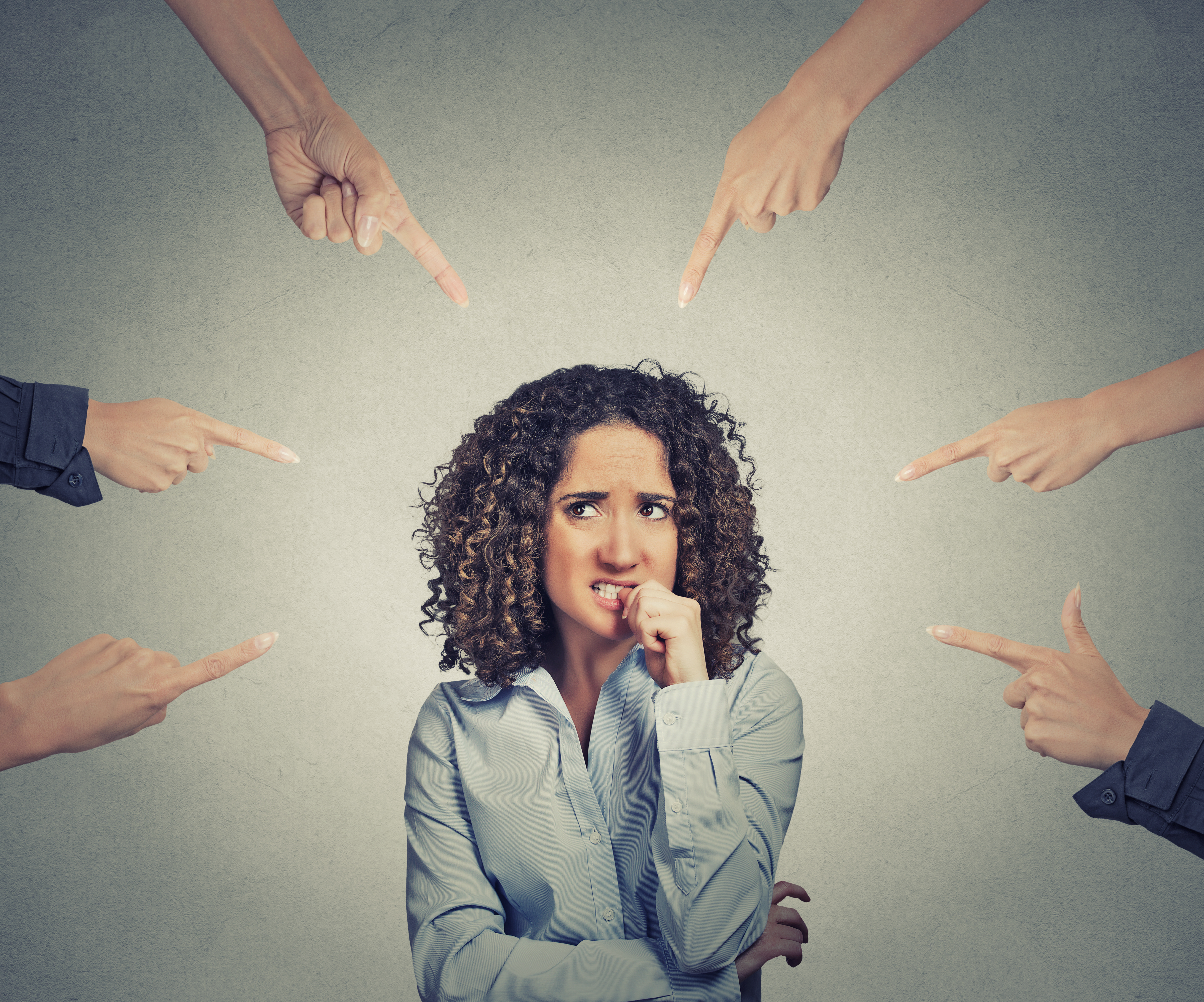 Anxious woman biting her nails while multiple hands around her point accusingly, symbolizing blame, pressure, or overwhelming judgment.
