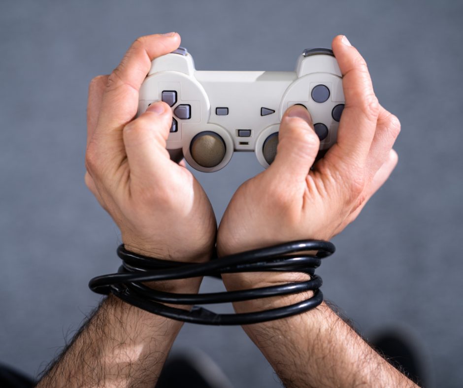 The image shows a person holding a white gaming controller with both hands, with their thumbs positioned on the sticks and buttons. The person has a black cable wrapped around their wrists, and the background is a plain, neutral gray.