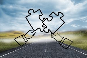 Two illustrated hands holding puzzle pieces that fit together, positioned over a long open road leading into the distance, symbolizing clarity, direction, and problem-solving.