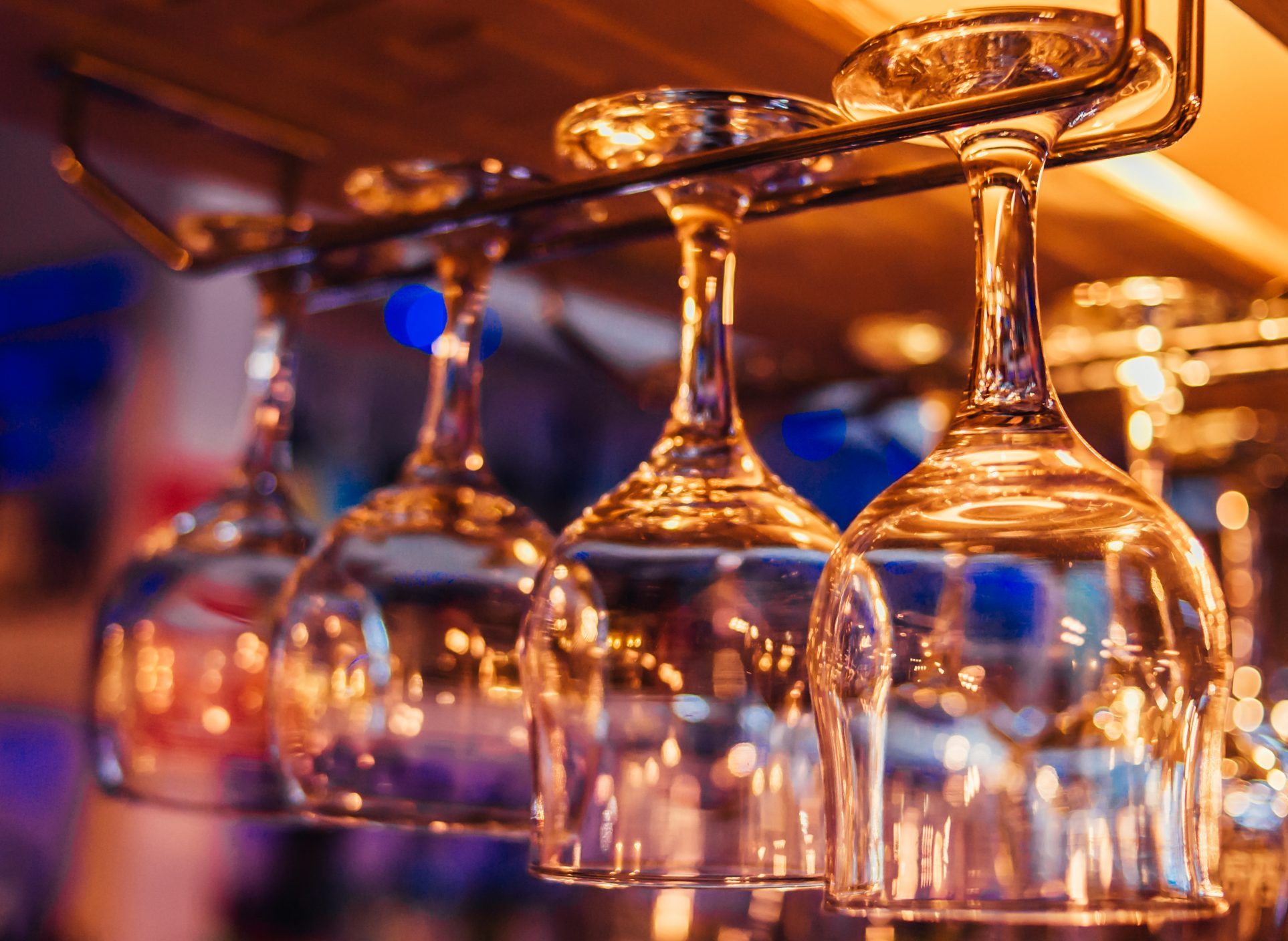 Several upside-down wine glasses hanging from a rack, illuminated by warm light.