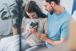Grieving couple sitting together as the woman gently holds a pair of tiny baby shoes, with the man comforting her during a moment of pregnancy or infant loss.