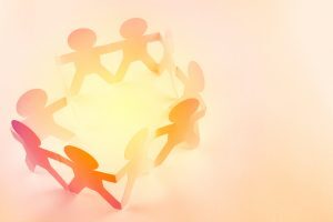 A paper craft of interconnected paper figures holding hands, arranged in a circle, with a warm, soft background. The figures are cut out of colored paper, creating a symbol of unity and togetherness.