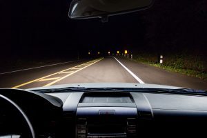 View from inside a car driving down a dark road at night, with headlights illuminating the lane and road markings ahead.