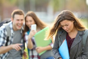 A man and a woman outdoors, with two smiling and taking a selfie while the woman looks down, holding a folder.