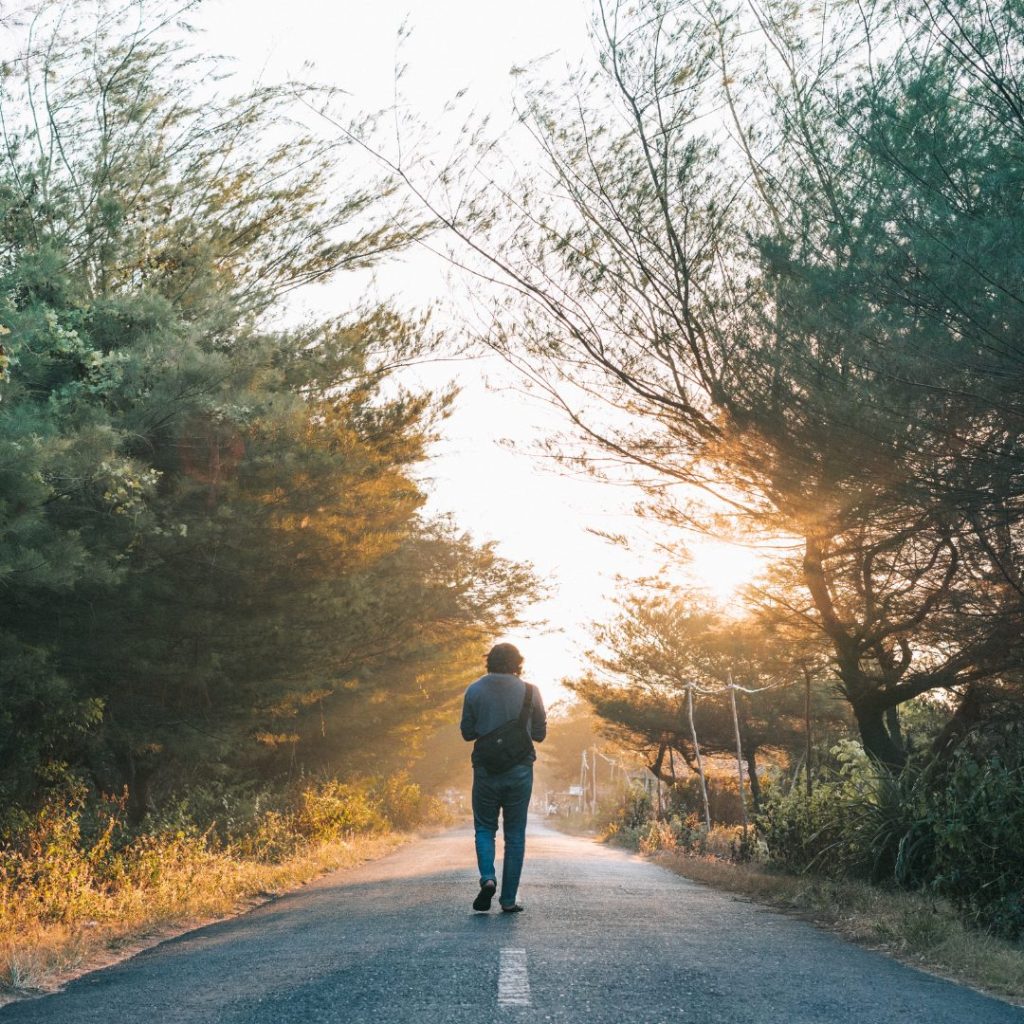 A lady taking a walk in the road in the woods.
