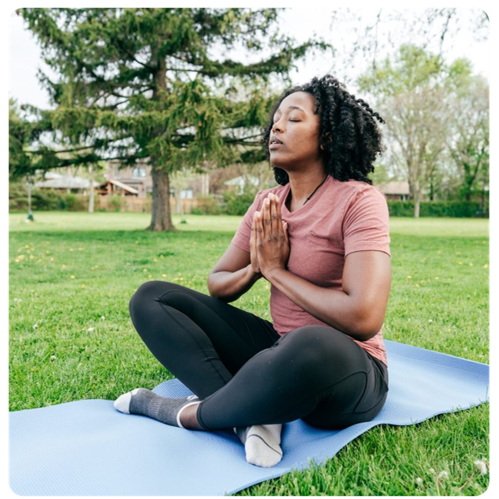 A lady with black curly hair sitting down and meditating.