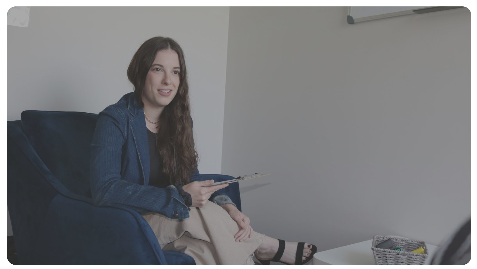 Hannah smiling and sitting, holding a clipboard.