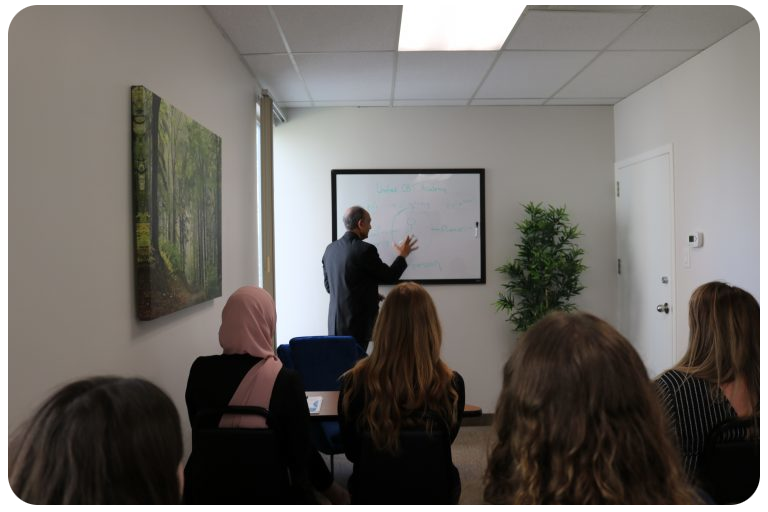 A group of people in a meeting with one man standing at the whiteboard.