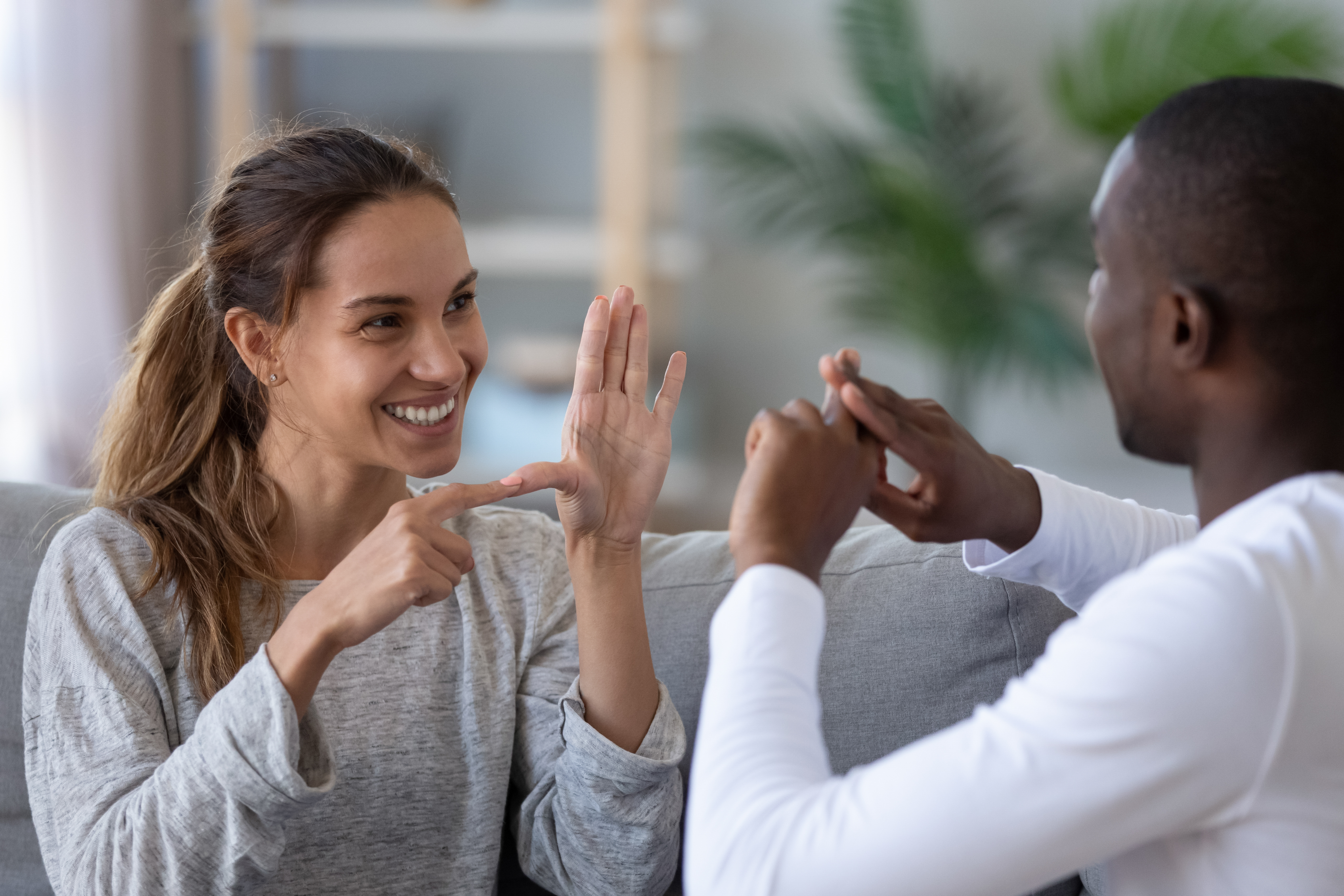Two people sitting together and smiling as they communicate using sign language, showing connection and understanding.