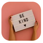 A person with red-painted nails holding a white lightbox against a pink background. The lightbox displays the message "BE KIND" with a small black heart symbol below. A person with red-painted nails holding a white lightbox against a pink background. The lightbox displays the message "BE KIND" with a small black heart symbol below.