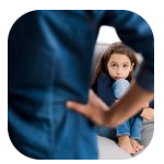 A young girl sitting on a couch, hugging her knees and looking up with a sad or troubled expression. In the foreground, an adult figure with crossed arms is partially visible, creating a sense of distance or confrontation between the two. A young girl sitting on a couch, hugging her knees and looking up with a sad or troubled expression. In the foreground, an adult figure with crossed arms is partially visible, creating a sense of distance or confrontation between the two.