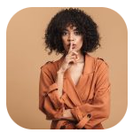A woman with curly dark hair and medium skin tone is standing against a beige background. She is wearing a rust-colored blazer with rolled-up sleeves and has her left arm crossed over her chest. She is holding her right index finger up to her lips in a "shh" gesture, suggesting silence or secrecy. A woman with curly dark hair and medium skin tone is standing against a beige background. She is wearing a rust-colored blazer with rolled-up sleeves and has her left arm crossed over her chest. She is holding her right index finger up to her lips in a "shh" gesture, suggesting silence or secrecy.