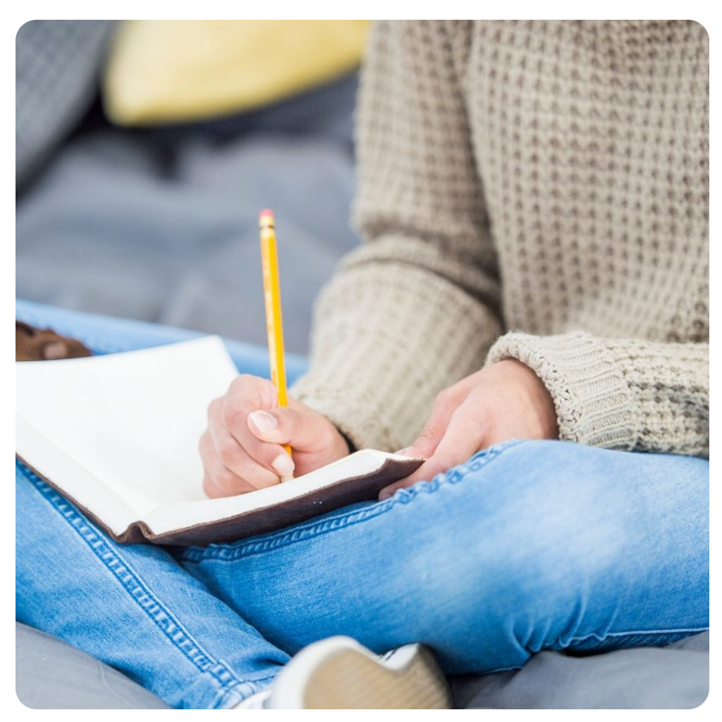 A lady sitting down wearing a sweater and blue jeans and writing in a notebook. A lady sitting down wearing a sweater and blue jeans and writing in a notebook.